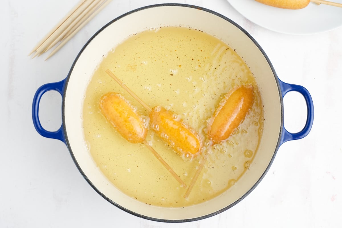 Three corn dogs frying in a pot of hot oil.