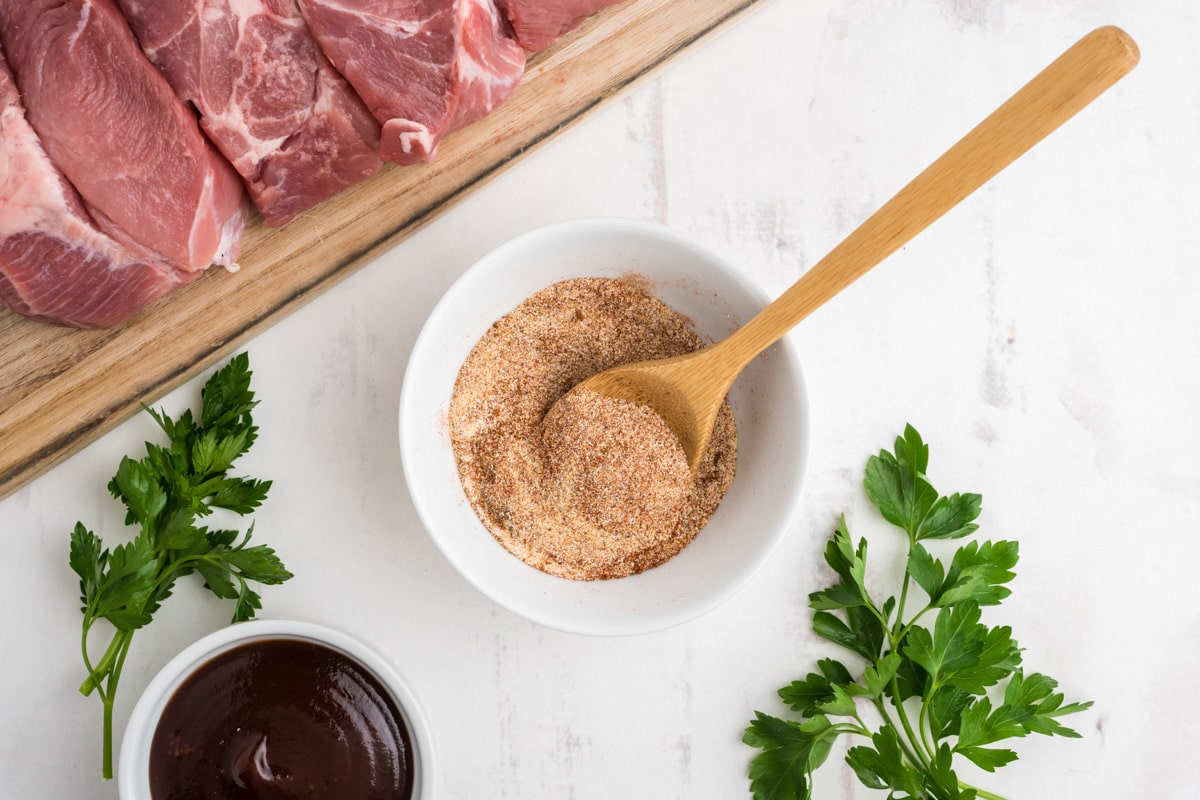 Spices mixed together in a small white dish with a small wooded spoon.