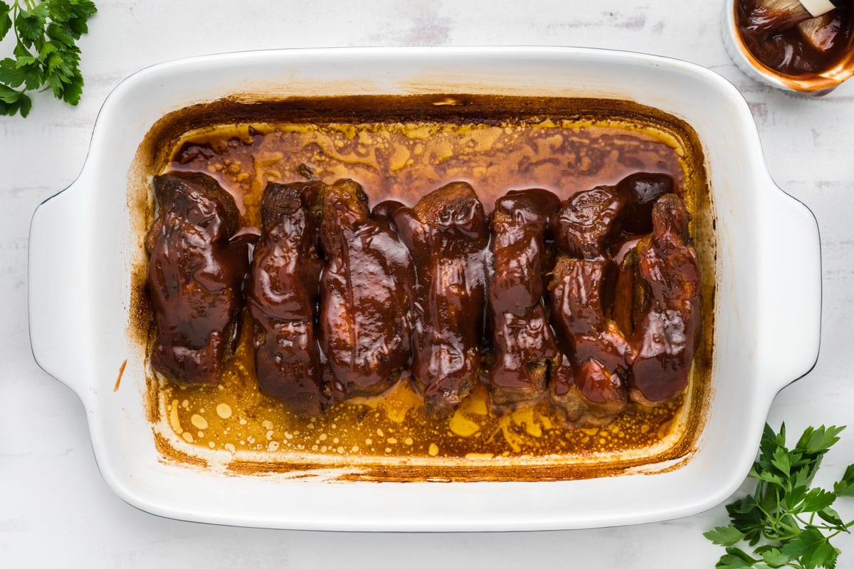 BBQ sauce covered boneless ribs in a white baking dish.