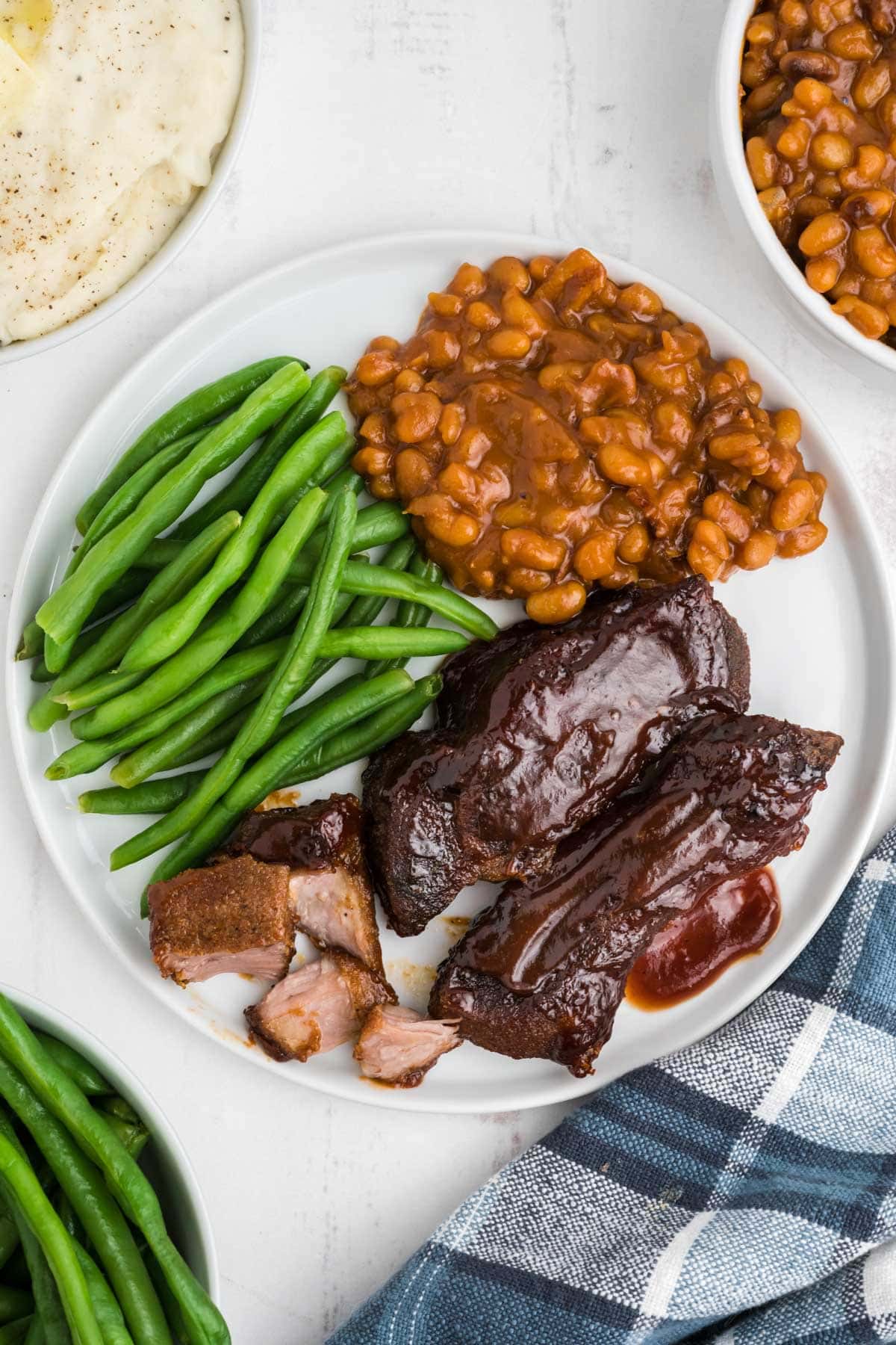 Country style ribs with bbq sauce, baked beans and green beans on a plate.