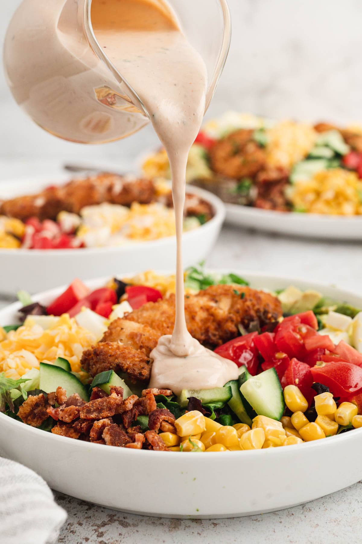 Salad in a bowl, dressing being poured on top.