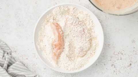 Chicken tenders in a bowl of panko breadcrumbs.