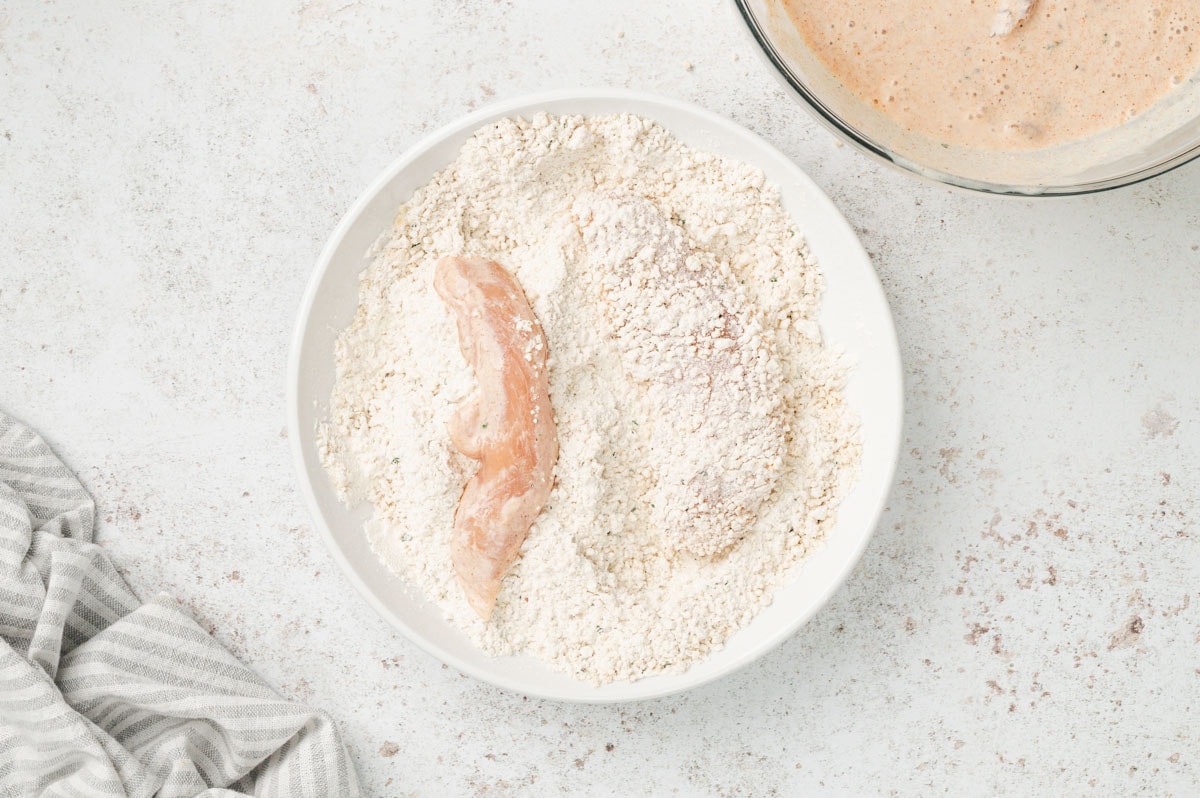 Chicken tenders in a bowl of panko breadcrumbs.