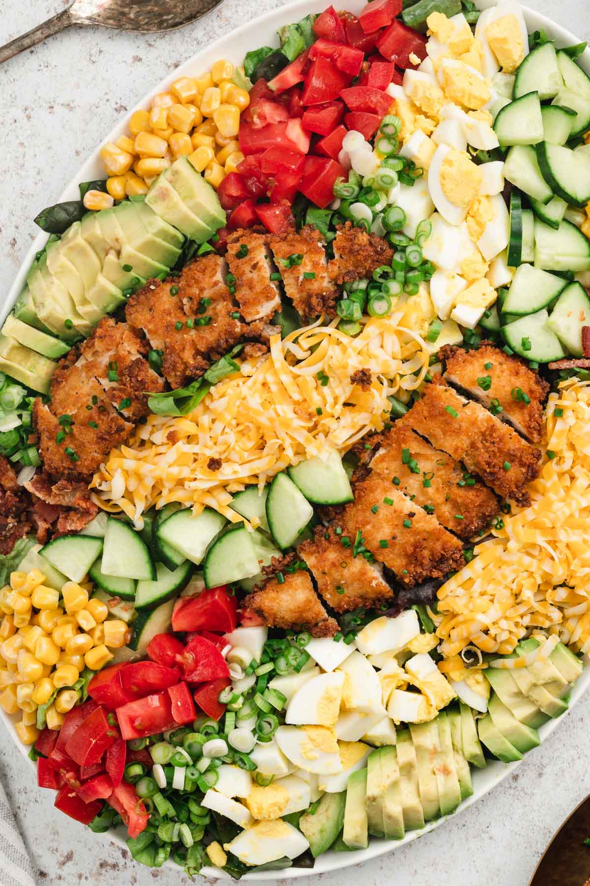 Lettuce on a platter, topped with hard boiled eggs, tomatoes, cheese corn and cucumbers and fried chicken.