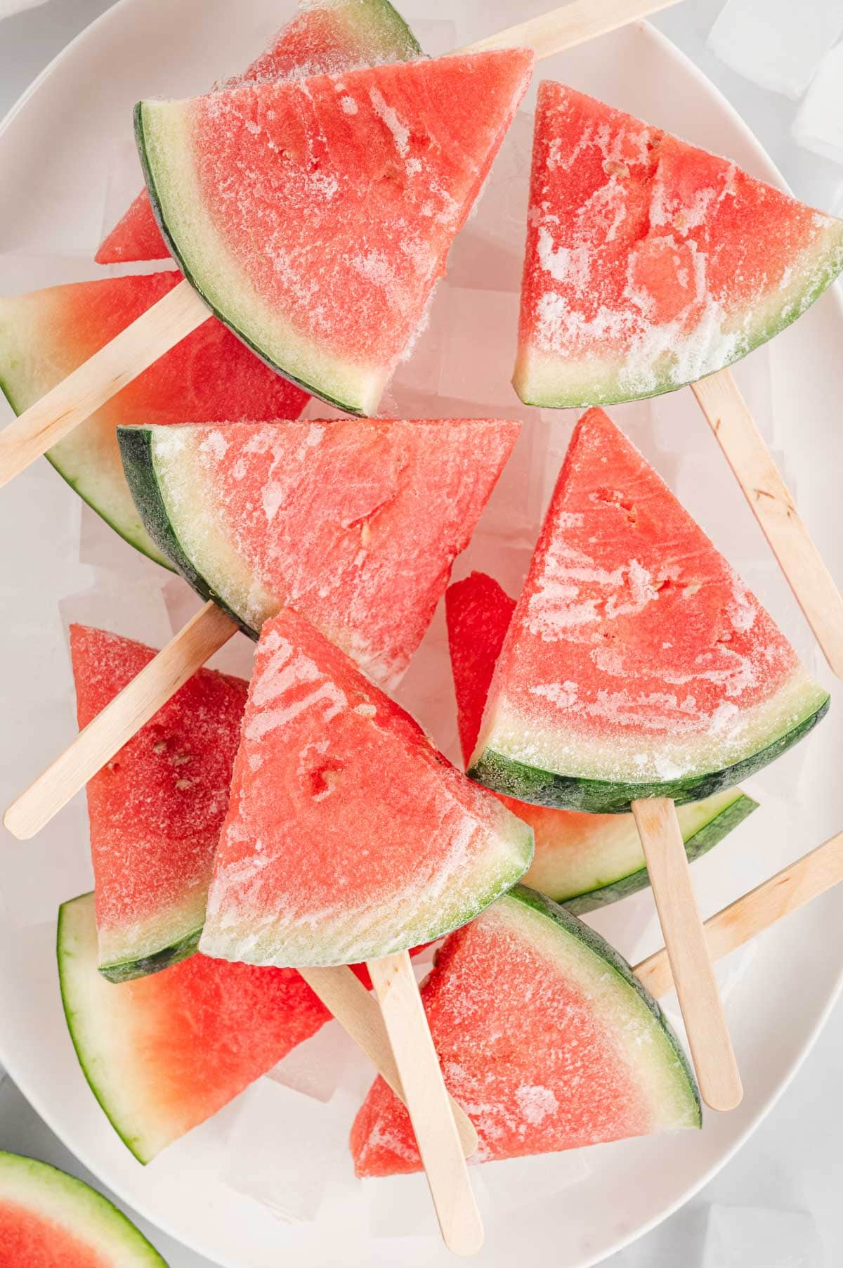 Triangular watermelon slices with popsicle sticks on a white platter. 