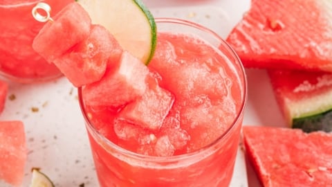 Watermelon slushy in a glass with a garnish of watermelon cubes and lime slices.