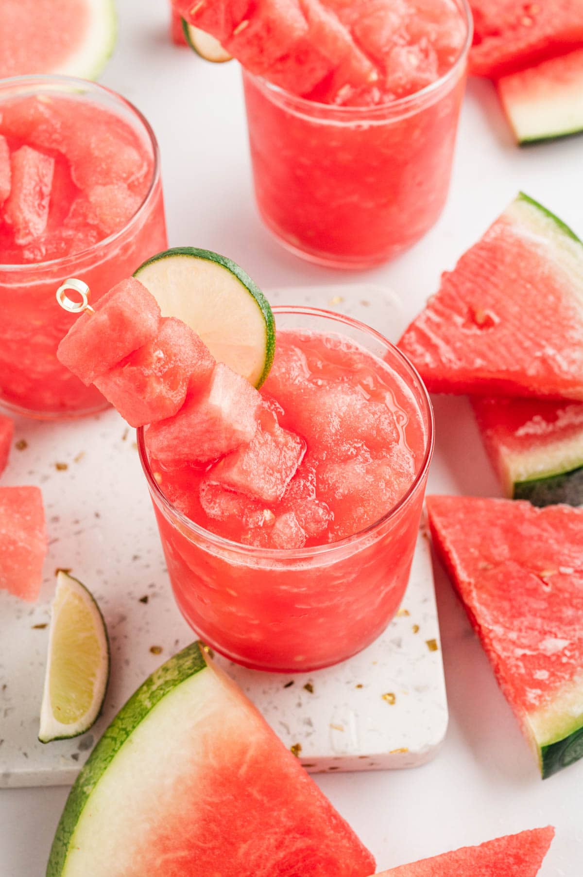 Watermelon slushy in a glass with a garnish of watermelon cubes and lime slices.