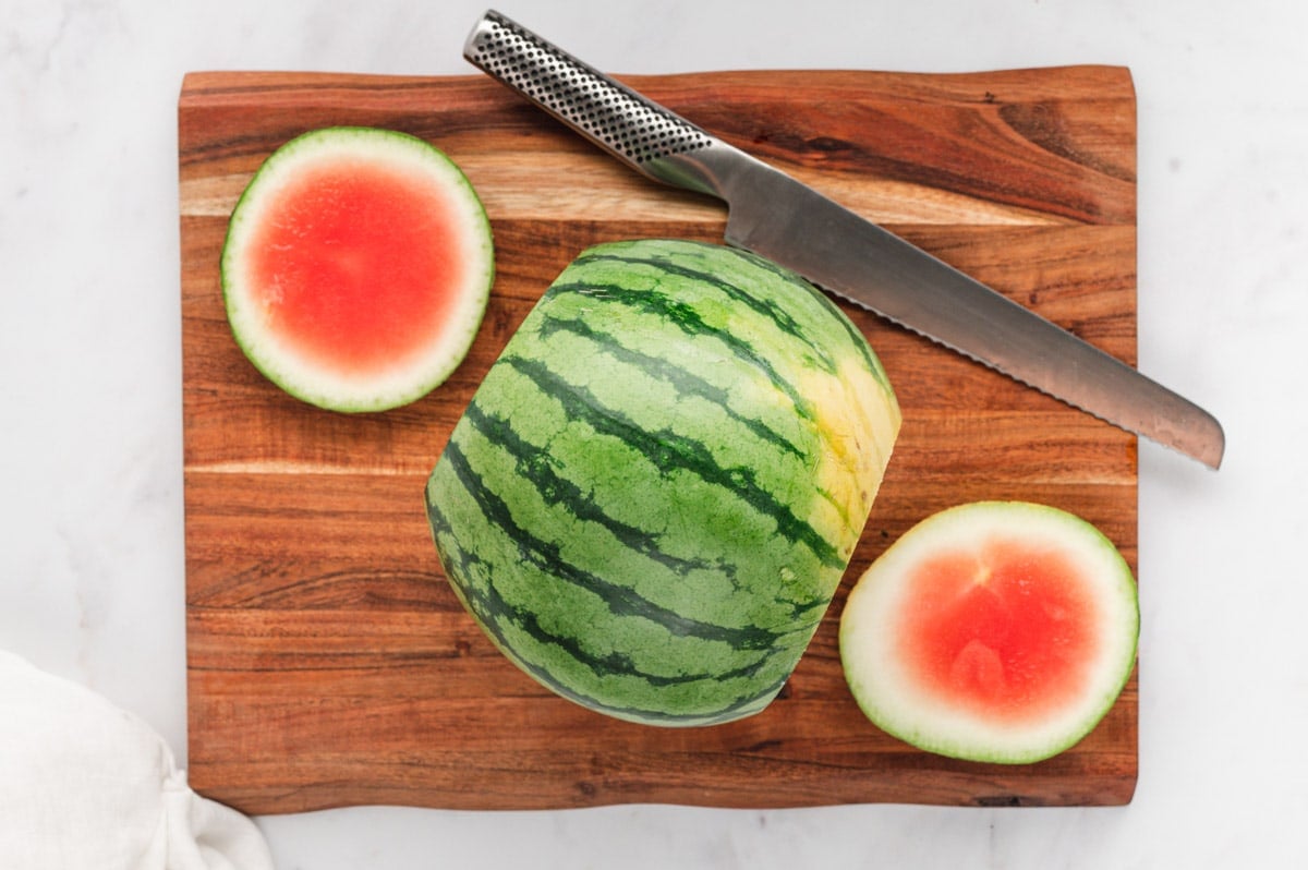 Watermelon on a cutting board, cut in half with the ends trimmed.