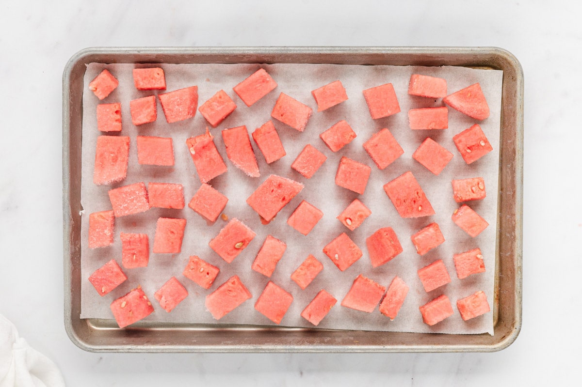 Frozen cubes of watermelon on a baking sheet with parchment paper.