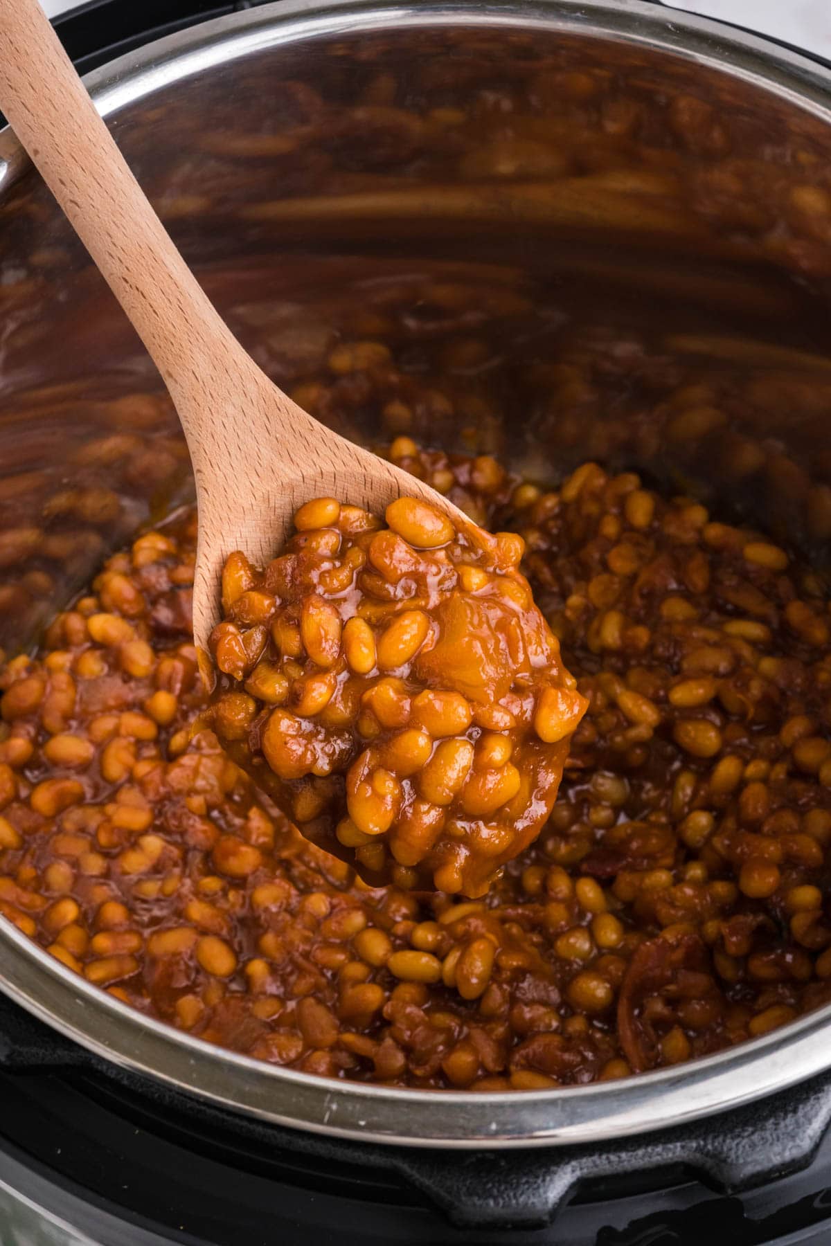 Baked beans in an instant pot, with a serving on a wooden spoon.