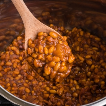 Baked beans in an instant pot, a serving on a wooden spoon.
