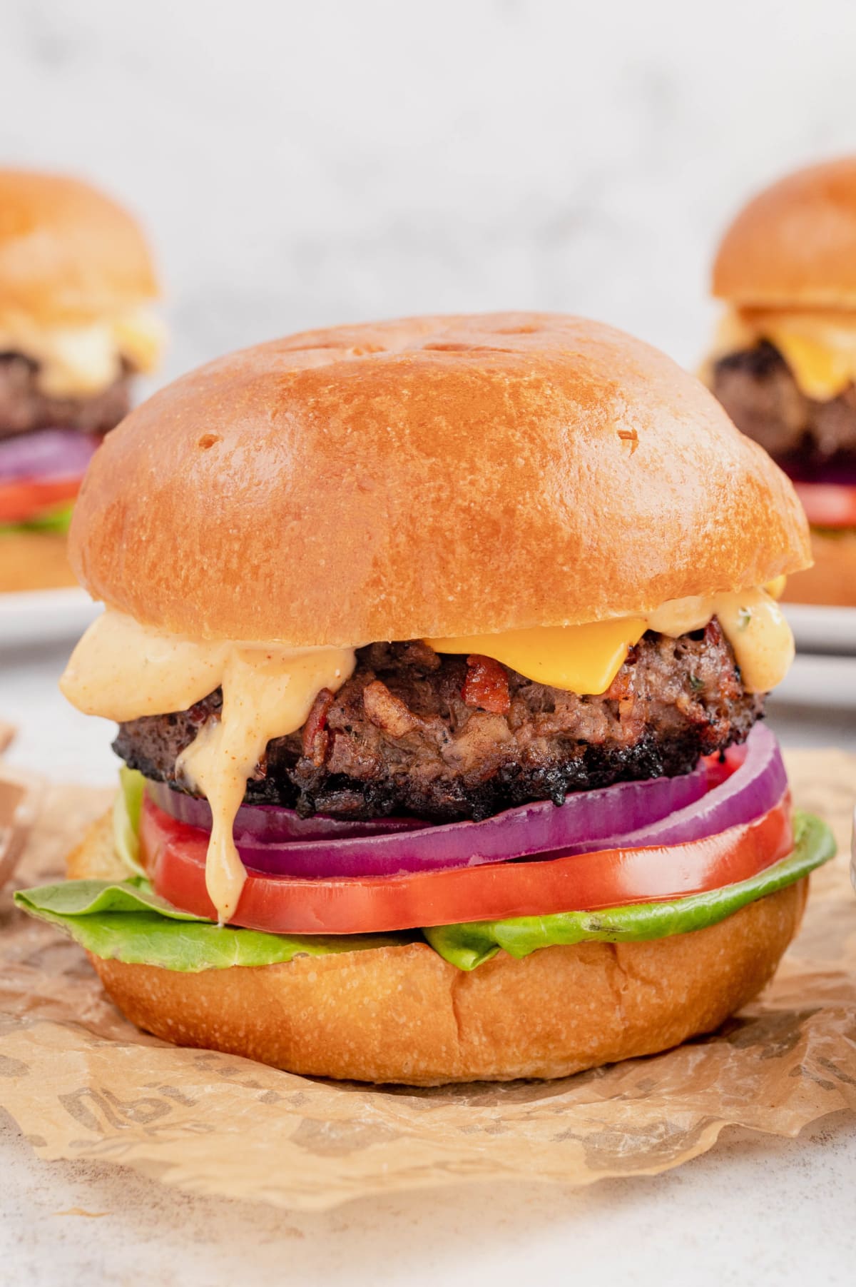 Tall cheeseburger with dripping sauce, onion, tomato and lettuce.