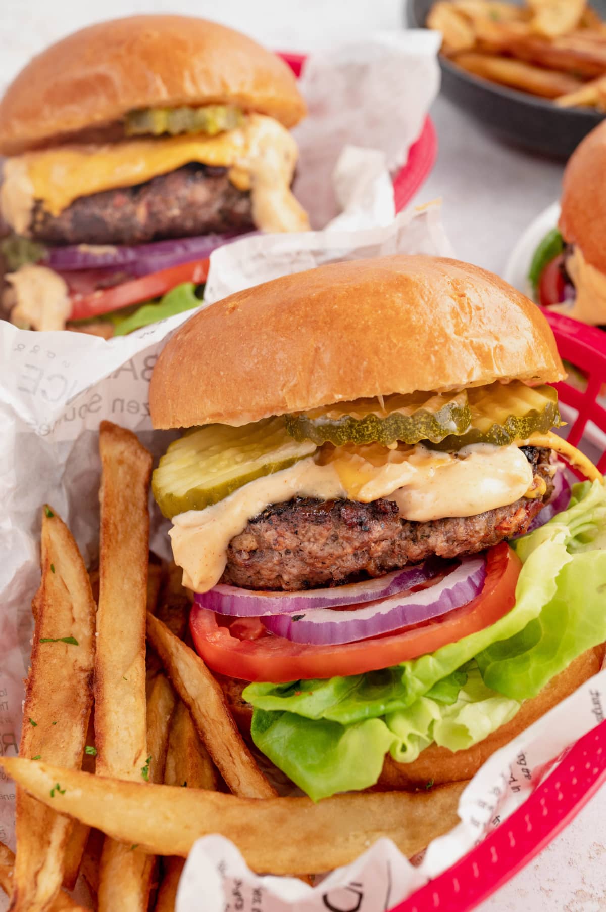 Cheeseburger with pickles, lettuce, tomato and onion in a red basket with french fries.