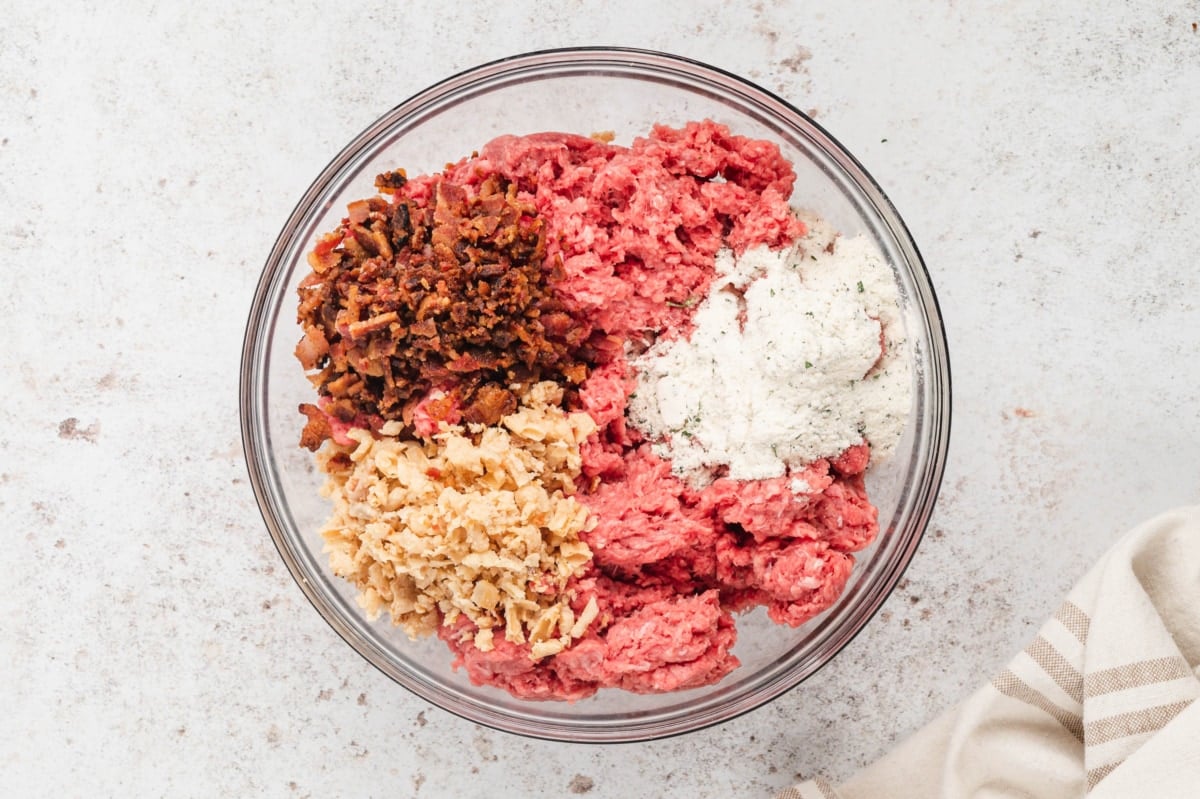 Ground beef, ranch seasoning, fried onions and bacon in a clear glass mixing bowl.