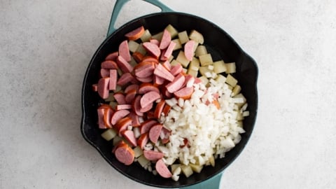 Sausage an onions over potatoes in a skillet.