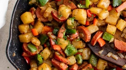 Large skillet filled with smoked sausage, potatoes, bell peppers and onions.