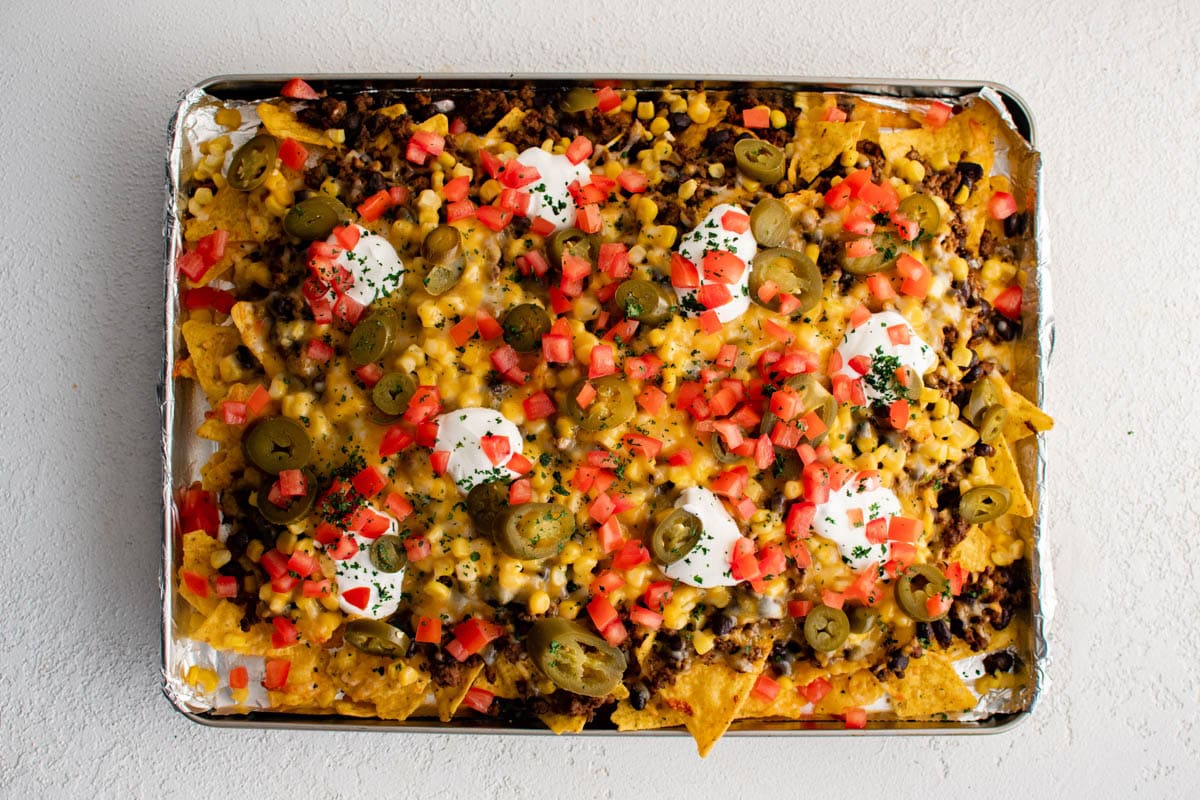 Loaded sheet pan nachos with sour cream, olives, tomatoes and jalapenos.