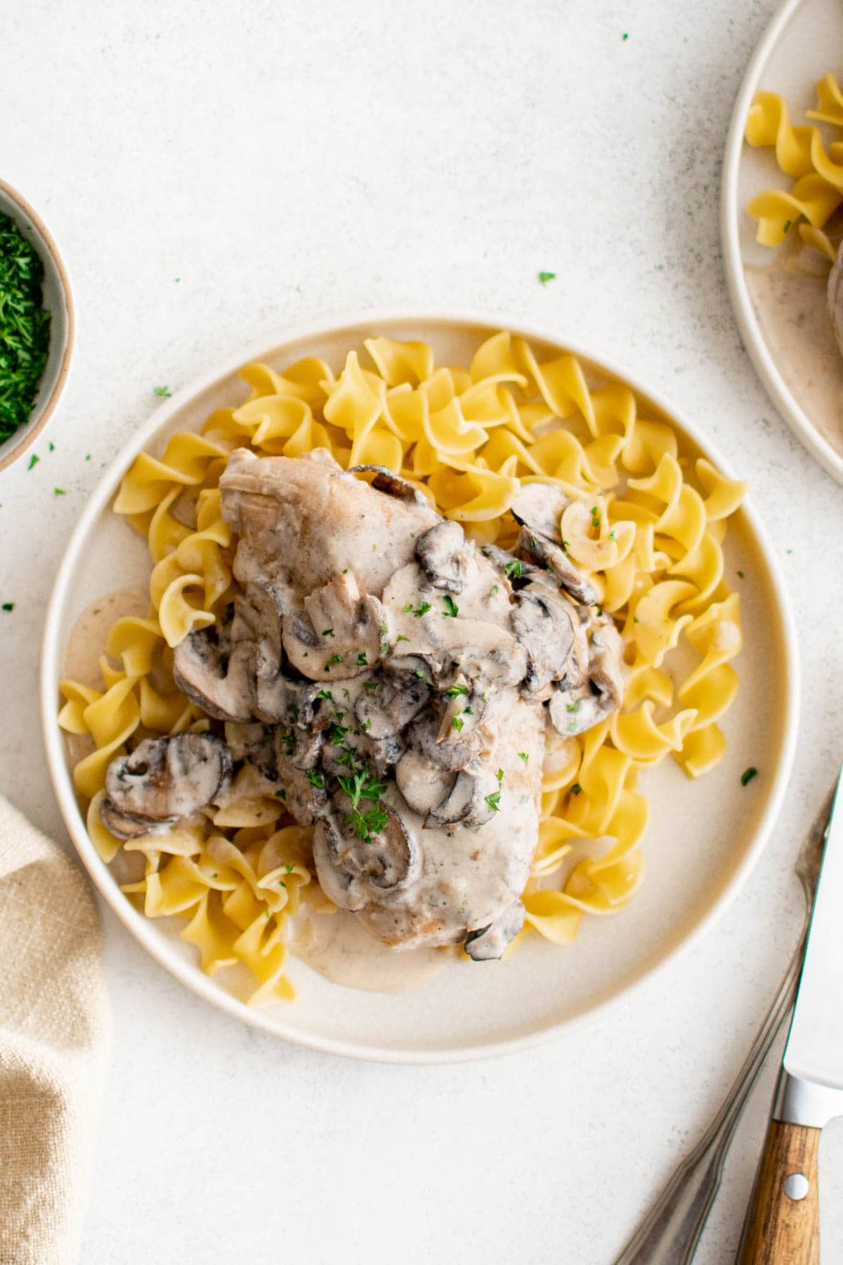 Chicken breast with mushroom gravy served over egg noodles on a white plate. 