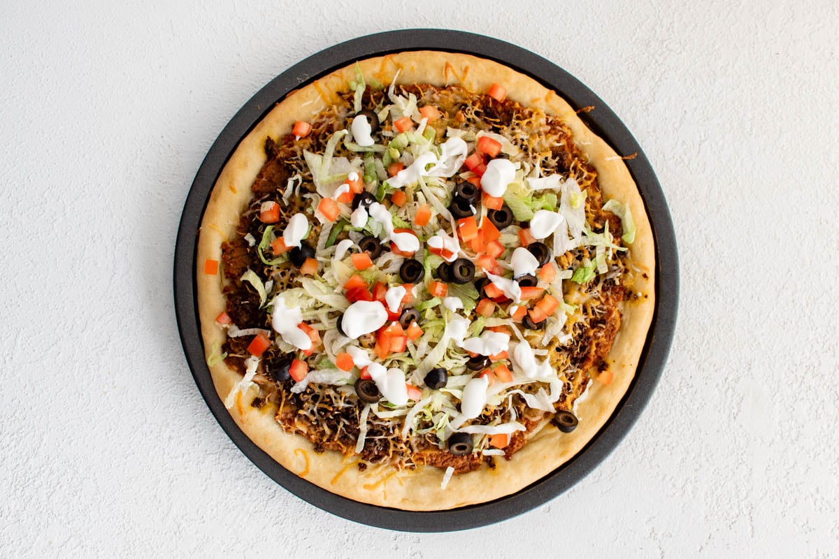 Taco pizza with beans, meat, cheese, lettuce, tomato and olives.