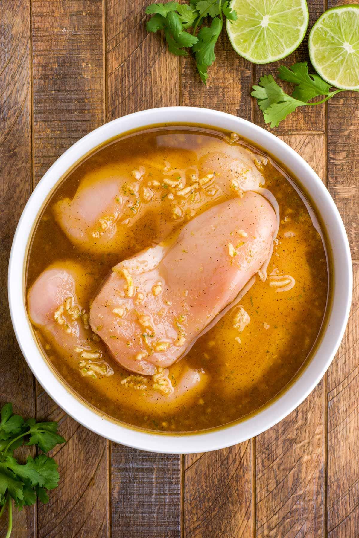 Chicken breasts sitting in a marinade in a bowl.