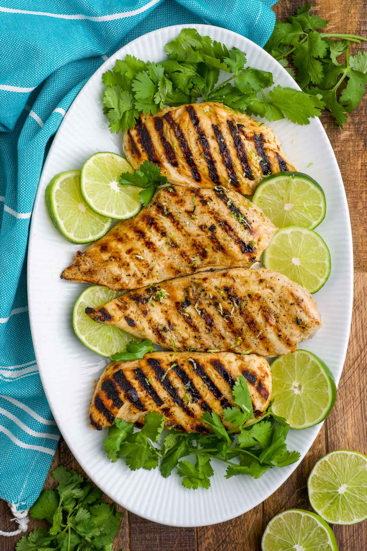 Grilled chicken on a white platter with limes and cilantro.