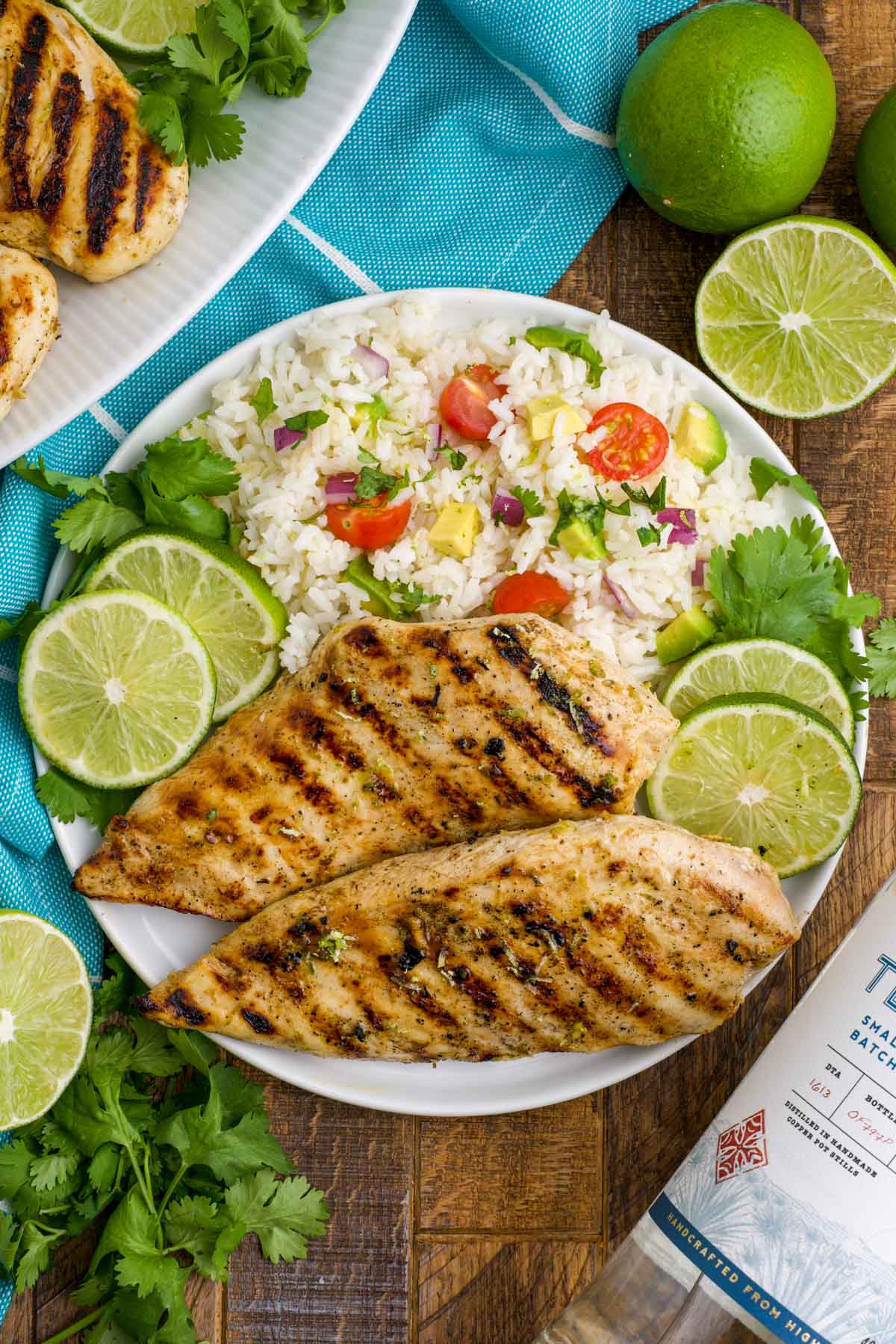 Grilled chicken breast on a plate with rice and tomatoes and lime slices.