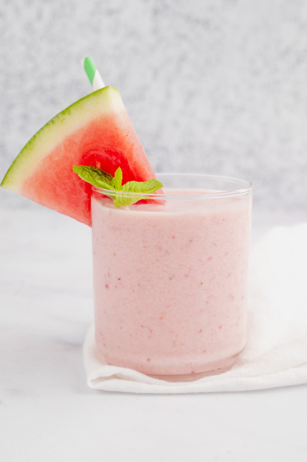 Pink watermelon smoothie in a glass with a watermelon wedge and a sprig of mint.