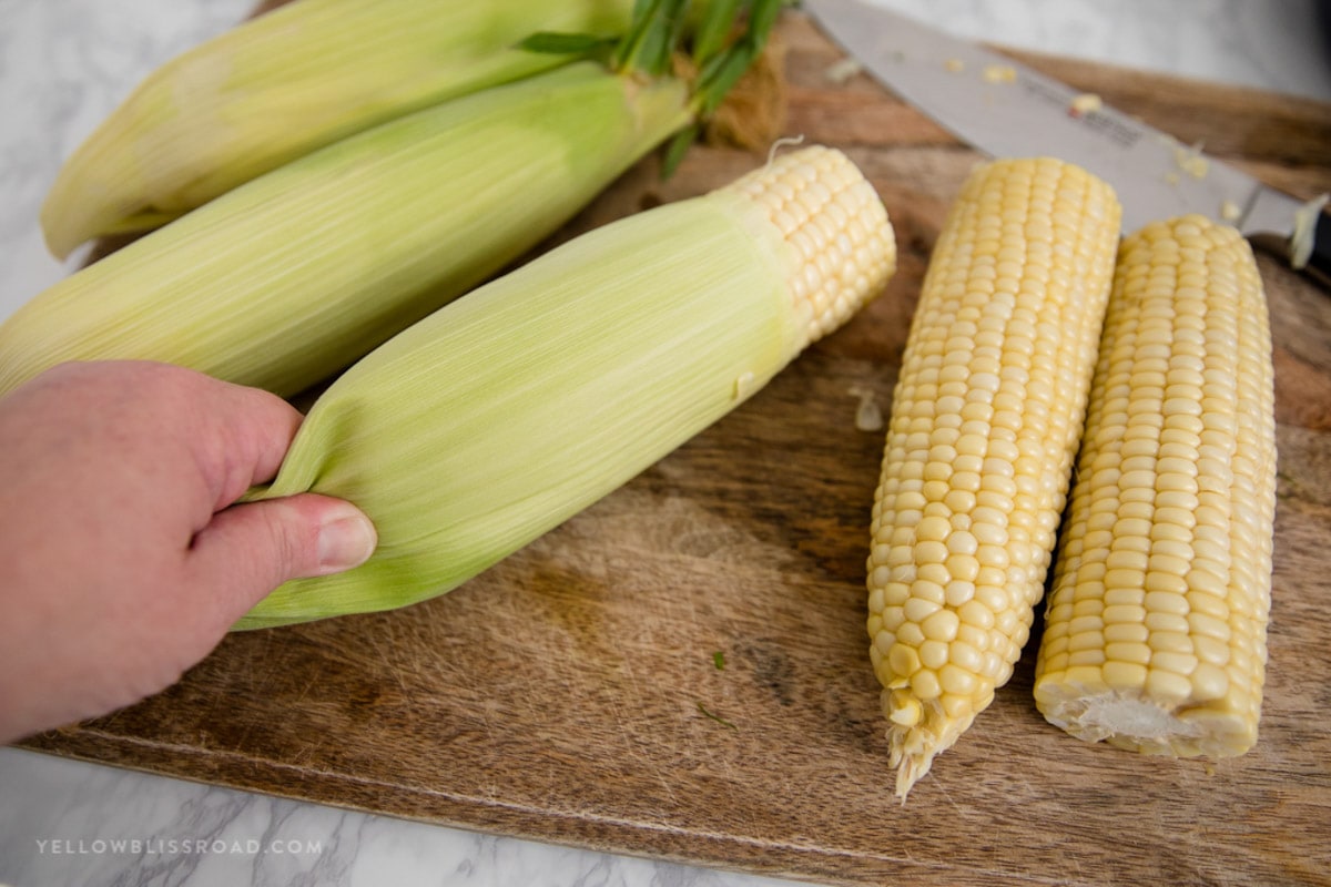 A hand removing a corn cob from it's husk.