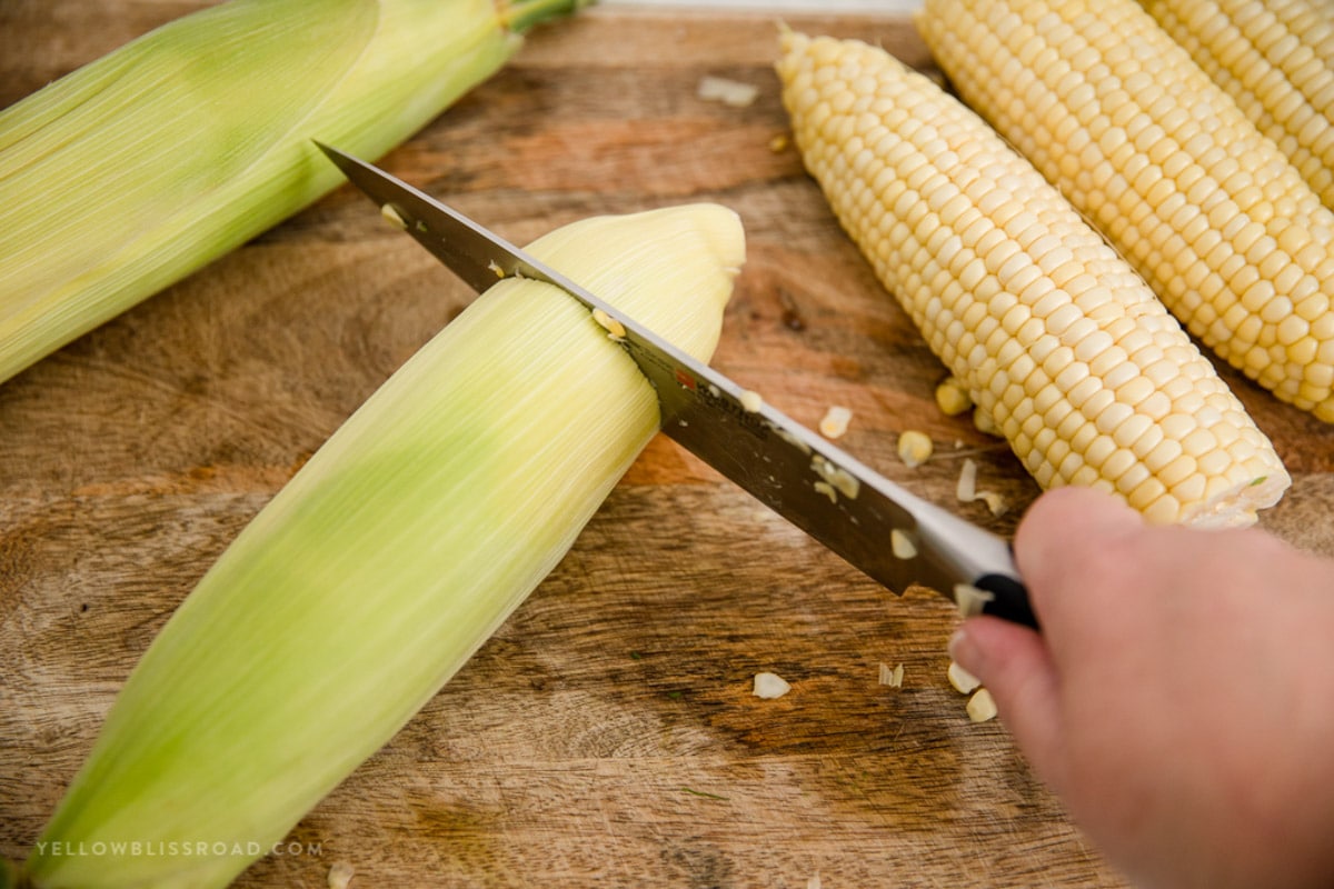 A knife being used to slice off the stalk end of a cob of corn.