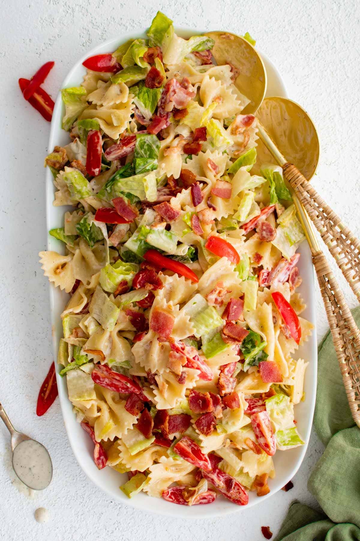 Platter with blt pasta salad and gold serving spoons.