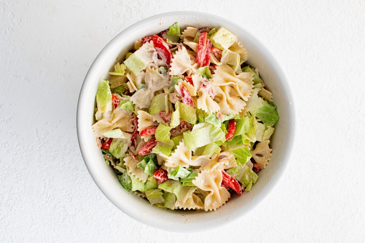 Lettuce, bacon, tomatoes and pasta in a white bowl.