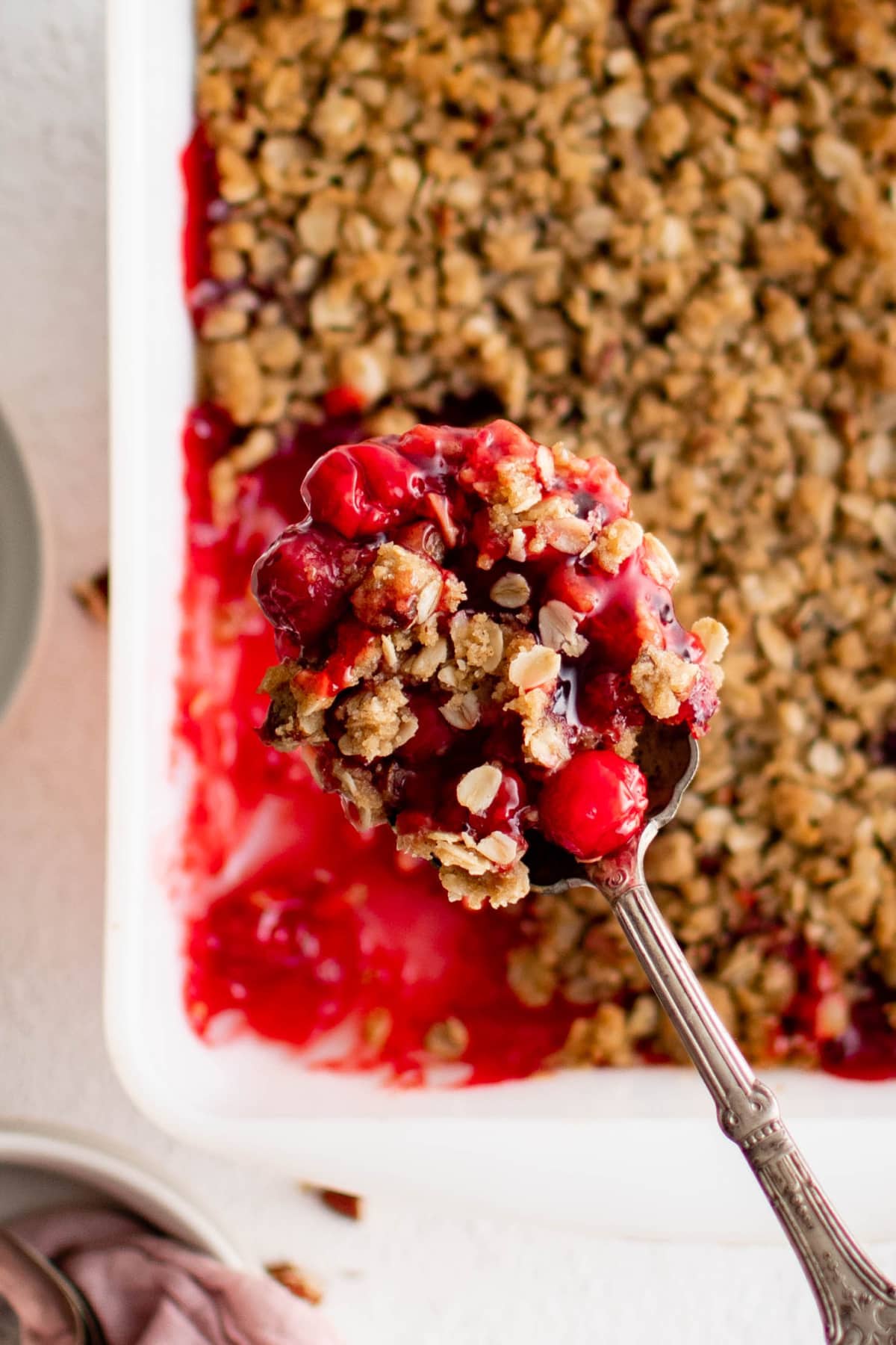 Cherry crisp, with a serving on a spoon held over the pan.