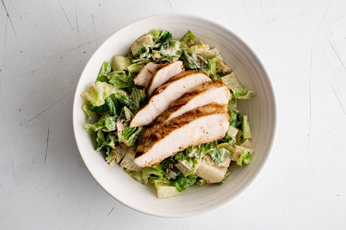 Dressed romain lettuce and sliced chicken in a white bowl.