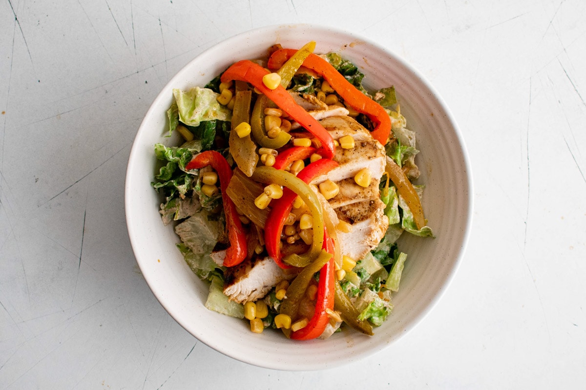 Salad with dressing, sliced chicken and cooked bell peppers and onions.