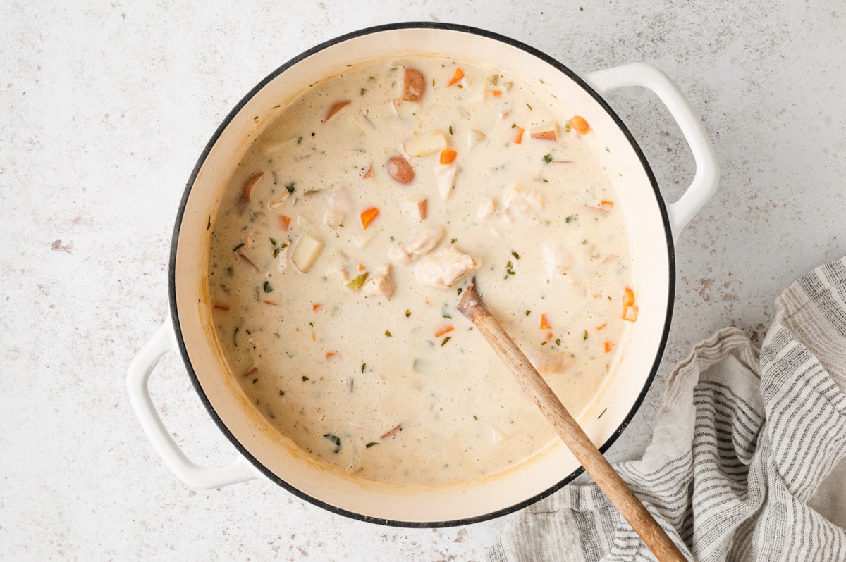 Creamy soup with veggies in a large soup pot with a wooden spoon.