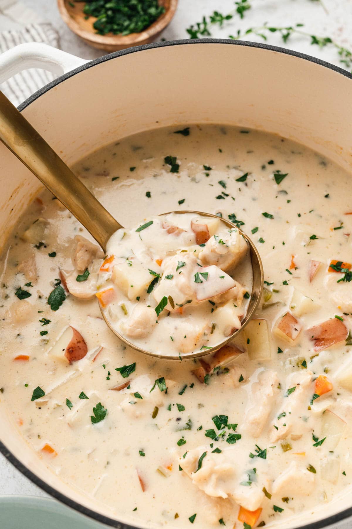 A creamy soup with chicken, potatoes and vegetables in a soup pot with a soup ladle.