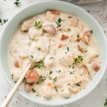 Chicken potato soup in a light blue bowl with fresh herbs and a small soup spoon.