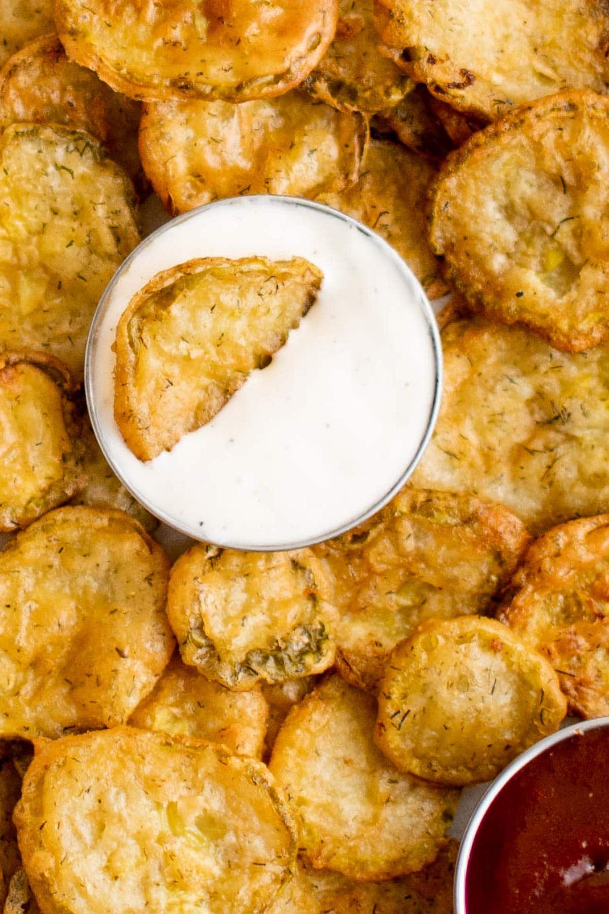 Fried pickles in a pile on a tray, with a small cup of ranch.