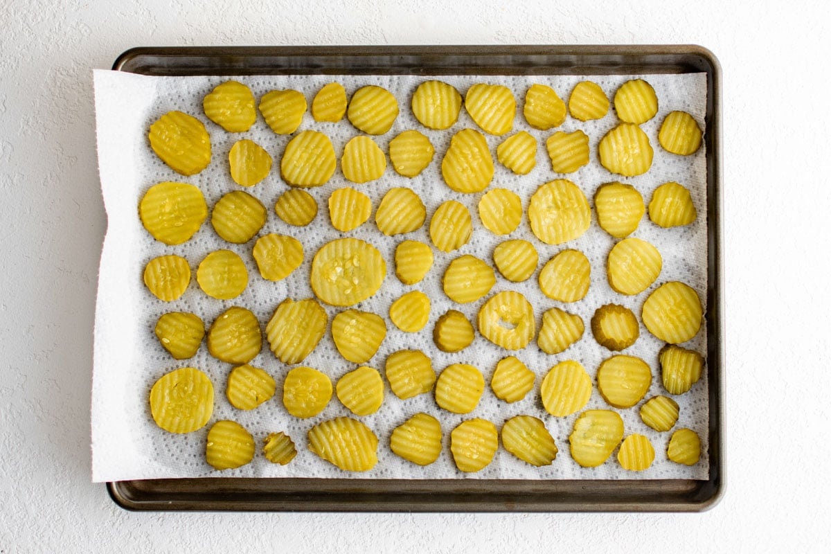 Dill pickle chips laid out on a paper towel lined baking sheet.