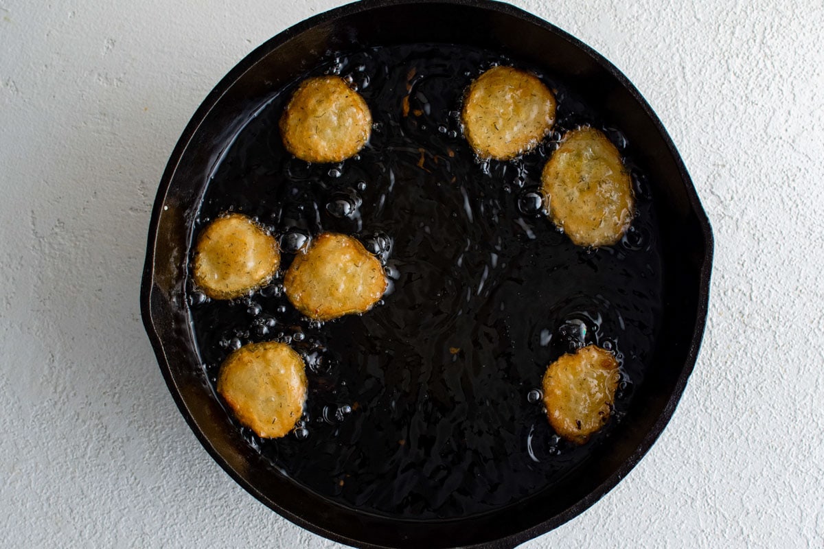 Battered pickles frying in a skillet.