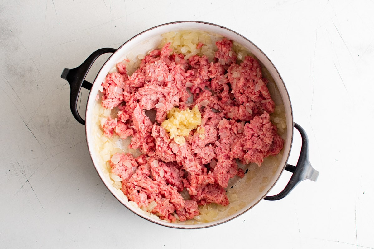 Raw round beef in a pan with onions and garlic.