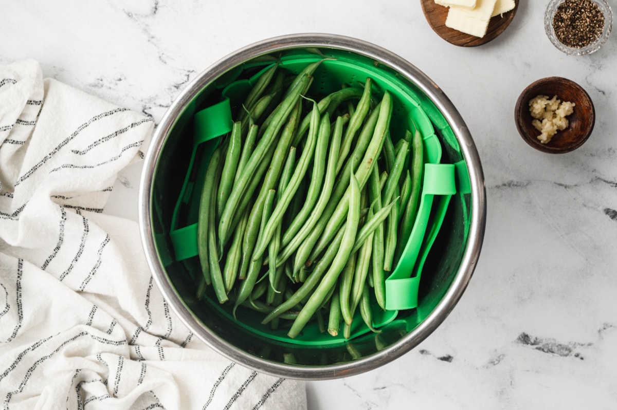 Fresh green beans in a green steam basket inside an instant pot.