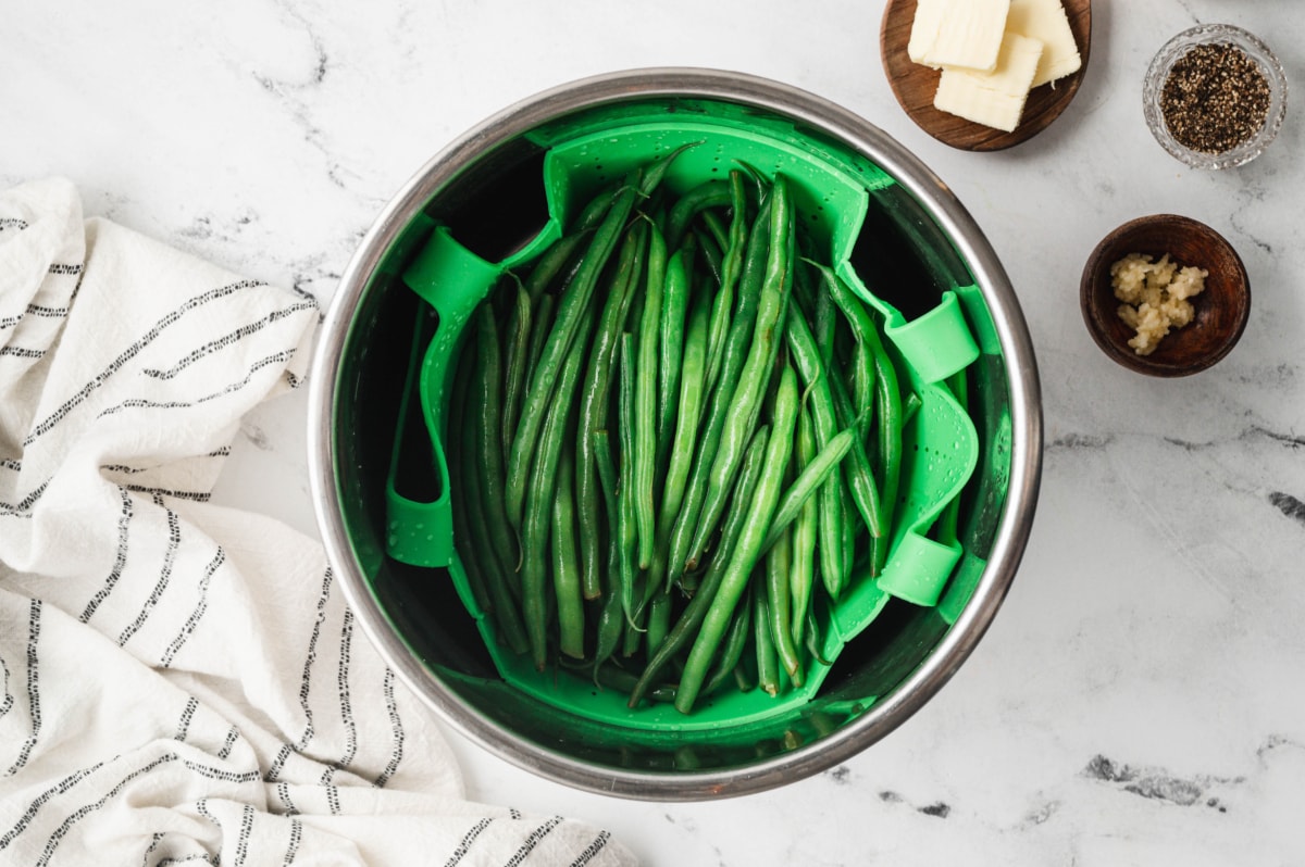 Cooked green beans in a green steam basket inside an instant pot.