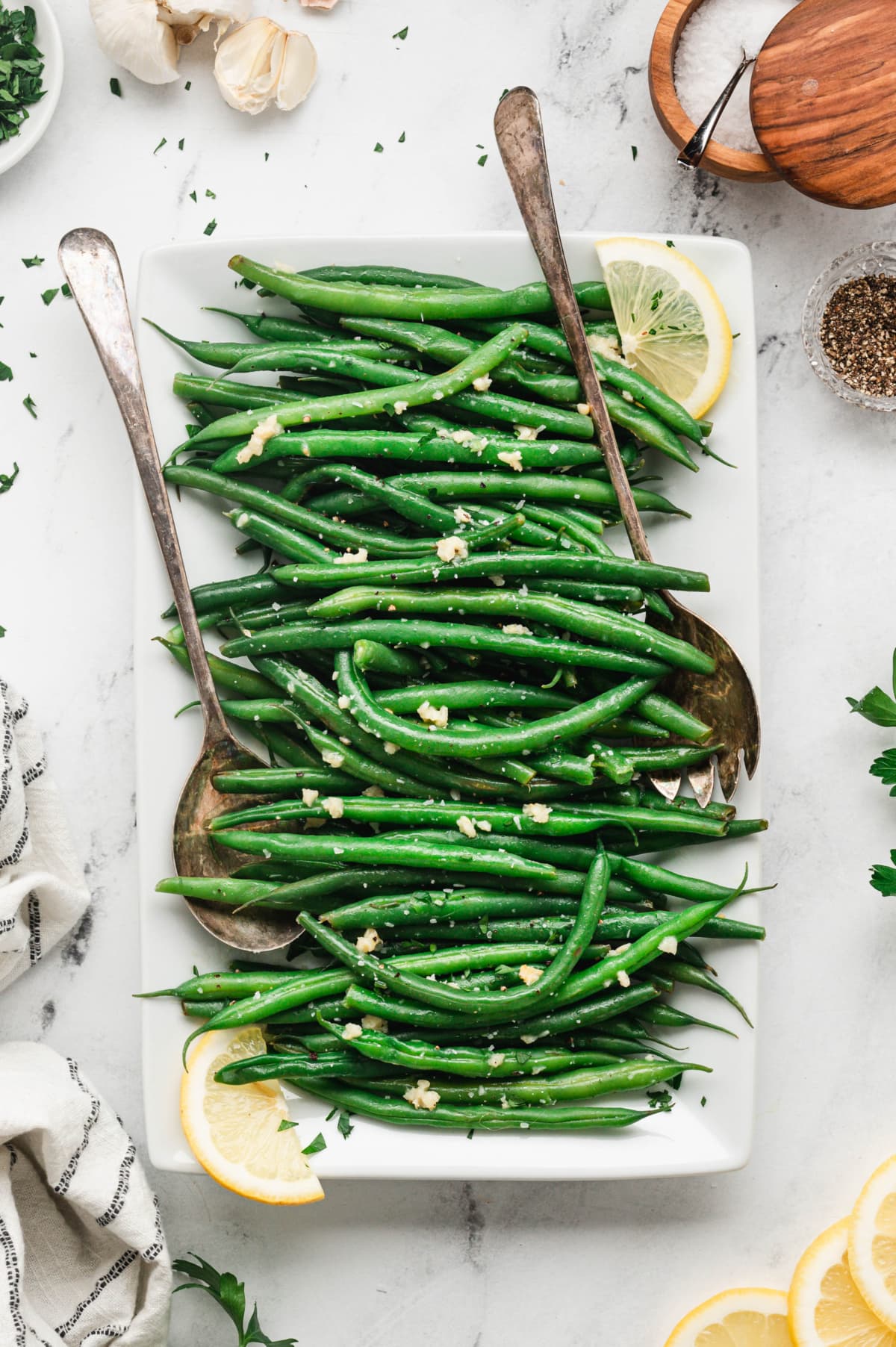 Green beans on a white platter with 2 serving spoons.