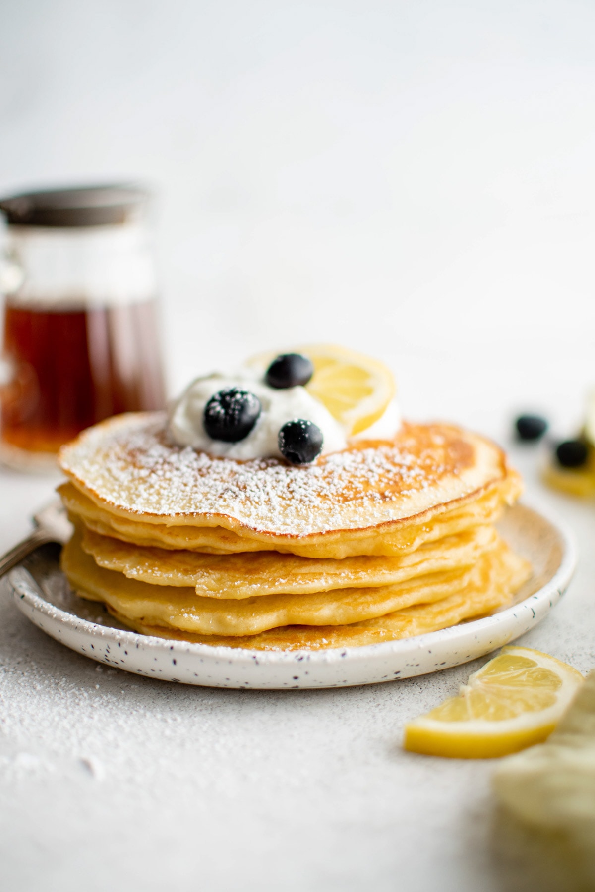 Stack of lemon pancakes, topped with whipped cream, powdered sugar and blueberries.