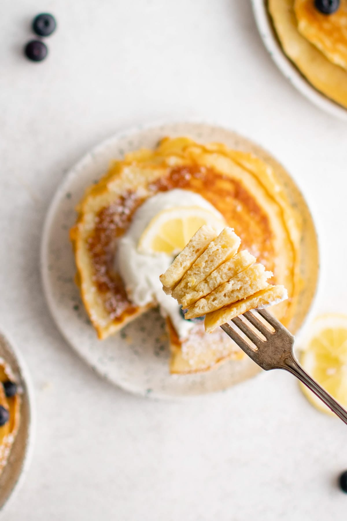 Lemon Pancakes with whipped cream and lemon zest, a fork with a cut bite of stacked pancakes.