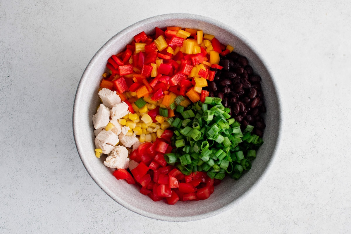 Fresh vegetables, tomatoes, corn, green onions and peppers and chicken in a bowl.