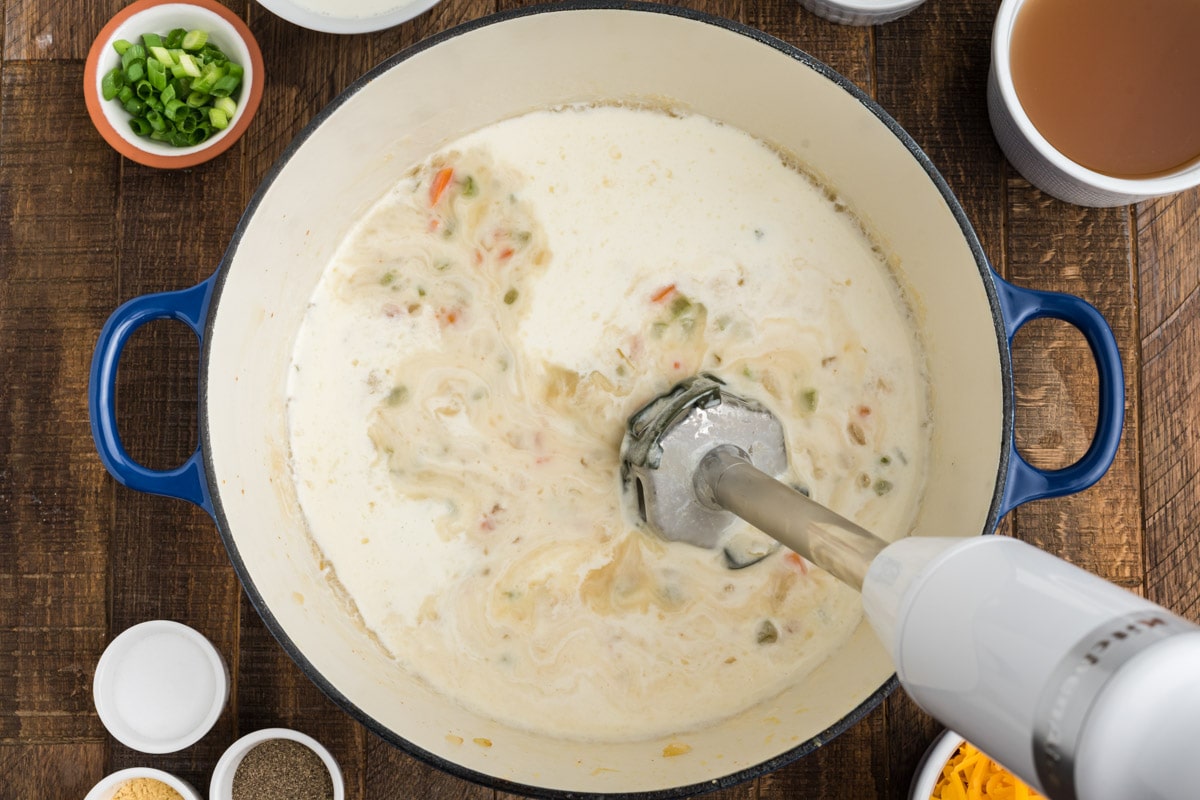 White soup with vegetables in a large pot, blending with an immersion blender.