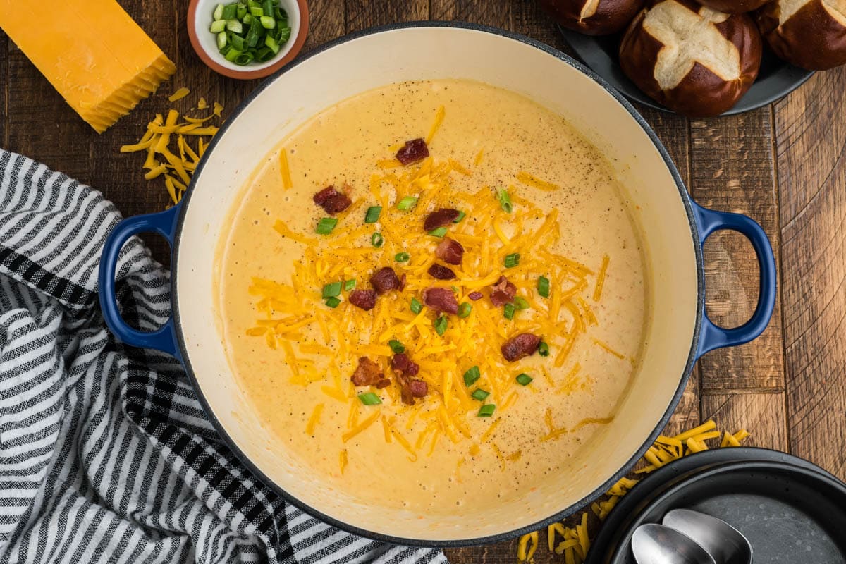 Large pot of beer cheese soup topped with shredded cheese, bacon and green onions.