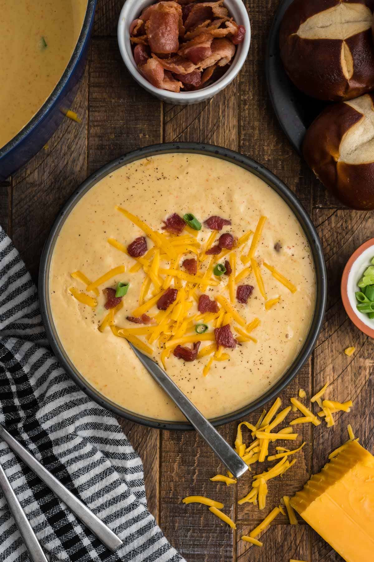 Cheesy soup in a black bowl and toppef with bacon bits, cheese and green onions with a small spoon.